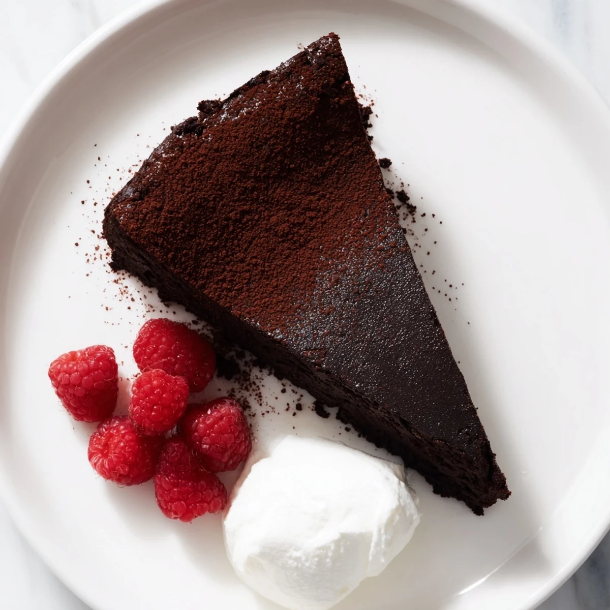 Slice of rich, dark, decadent flourless chocolate cake with a dusting of cocoa powder and fresh berries.