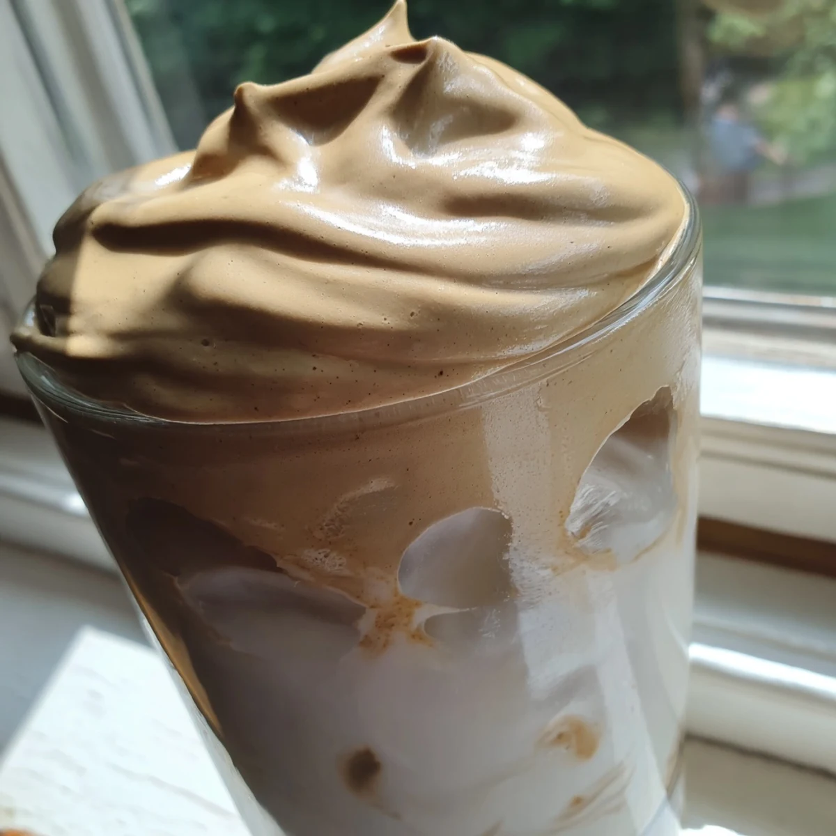 Two glasses of homemade Dalgona coffee are ready to serve with a straw, showcasing its thick, frothy texture.