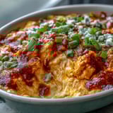 Hot and creamy Buffalo Chicken Dip scooped onto a blue corn chip, showing shredded chicken and tangy red sauce, next to crisp celery.