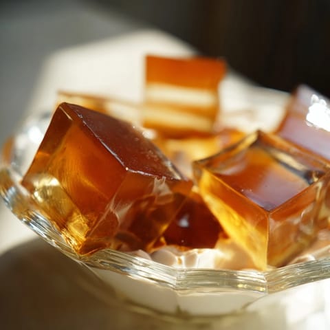 Homemade coffee jelly cubes are spooned into a serving glass, ready to be topped with vanilla-sweetened heavy cream.