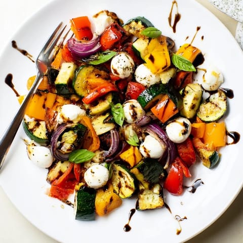 A vibrant Roasted Veggie Caprese Salad served warm, featuring caramelized cherry tomatoes and fresh basil on a platter.