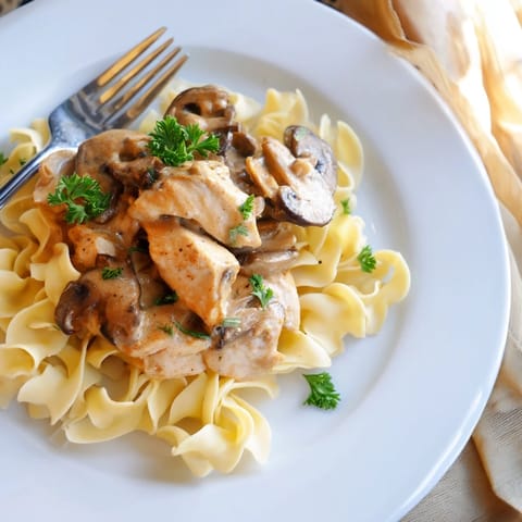 Steaming platter of homemade Chicken and Mushroom Stroganoff features earthy mushrooms, juicy chicken, and a velvety sour cream sauce served atop buttery egg noodles.