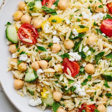 Lemony Chickpea Orzo Salad served in a glass bowl, packed with cucumber, tomatoes, and fresh herbs.