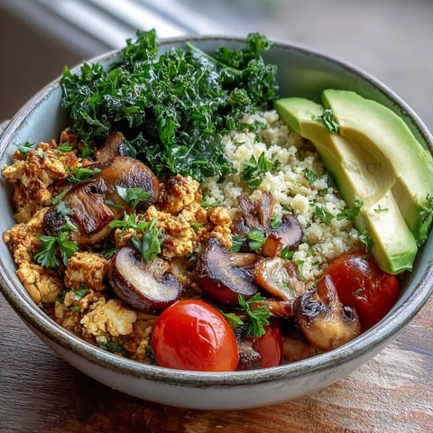 Golden scrambled tofu with sautéed mushrooms and kale over a fluffy whole wheat couscous base, garnished with fresh parsley and avocado slices.