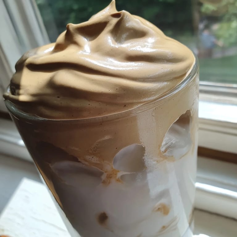 Two glasses of homemade Dalgona coffee are ready to serve with a straw, showcasing its thick, frothy texture.