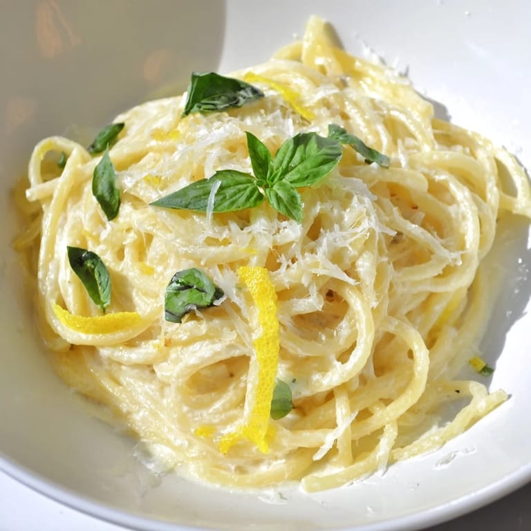 Bright lemon ricotta pasta twirled on a fork, garnished with black pepper and a glass of crisp white wine.