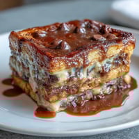 A warm, golden chocolate croissant bread pudding with melted chocolate pockets and a crisp top, served in a white baking dish.